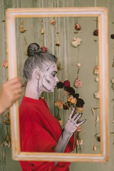 骷髅脸艺术妇女 手拿框架 室内肖像画靠着挂满干花的装饰墙 — 图库照片