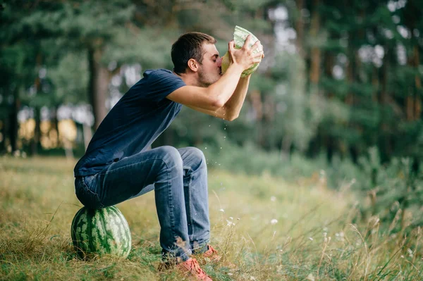 Young odd strange man eating watermelon and drinking its juice at nature. Great delicious taste of summer fruit. Funny adult male fooling with food outdoor in woods. Healthy useful natural  nutrition.