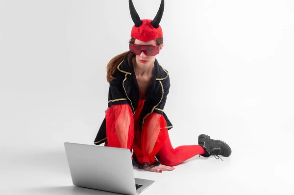 セクシーブルネット女性で赤タイツ 黒ブーツと悪魔角でラップトップ以上ホワイトスタジオ背景 — ストック写真