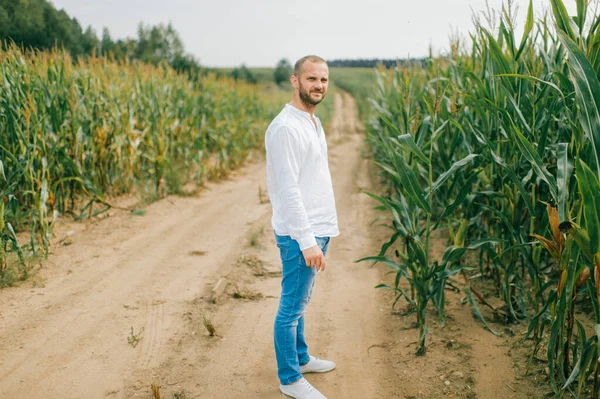白いシャツを着た美しい若い白人男性 青いジーンズと白いブーツは トウモロコシ畑で散歩に行きます — ストック写真