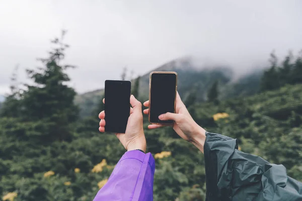 Goverla, Ukraine - July 14, 2018: travelers hands with smartphones take picture of nature landscape view in summer rainy day. Ttourists in camping adventure take selfie with cellphones. Happy moments