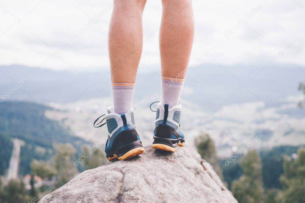 Mood photo of male legs wearing sportive hiking shoes with strong protective sole. Mens legs in trekking footwear for mountain travel standing on stone outdoor at nature on abstract background