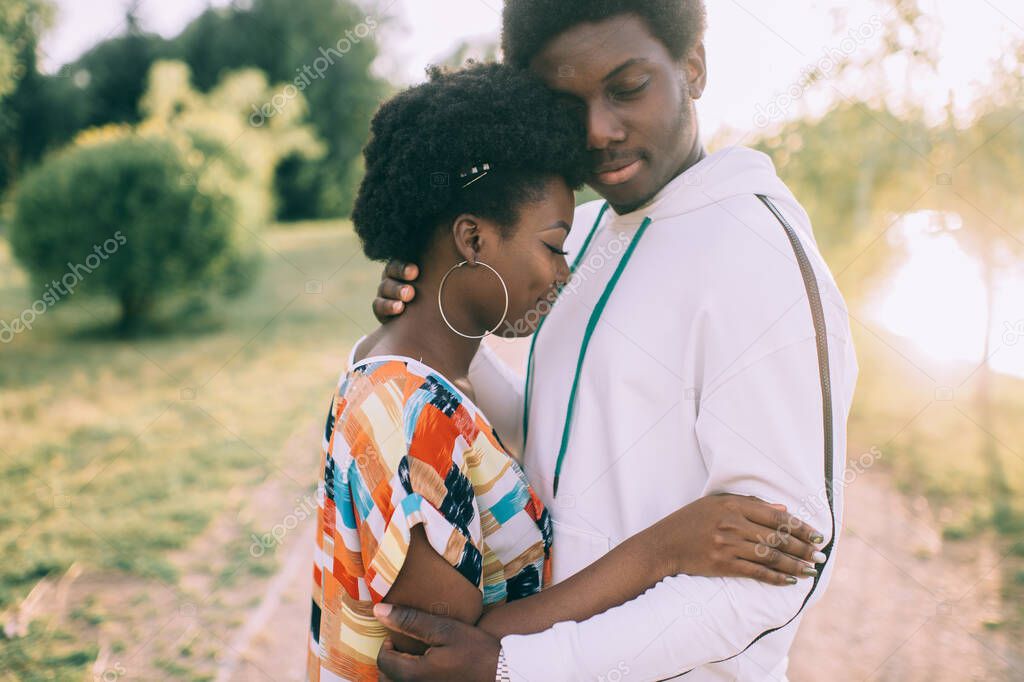 Beautiful african american loving couple with smiling faces hugs outdoor in autumn park at sunset