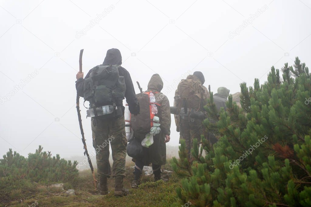 Hiking. Backpackers hiking up the foggy mountains. Mountain trekking. Men with backpacks on trek