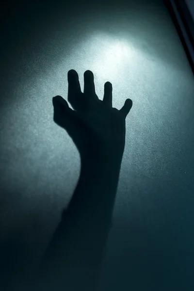 Silhouette of horror hand behind frosted glass