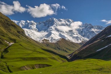 Güzel bir bahar gününde karla kaplı güzel dağlara ve yeşil vadilere bak.