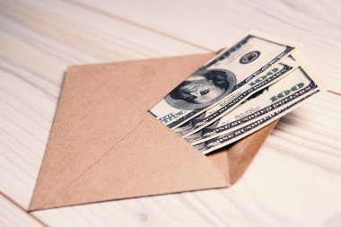 Tahta bir masanın üzerindeki zarfın içinde Amerikan doları. Gelir, ikramiyeler veya rüşvet konsepti.
