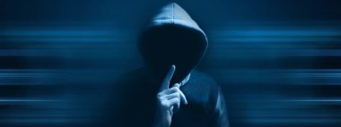 Kapüşonlu adam sessizlik hareketi yapıyor.