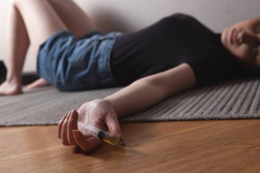 Kız yerde yatıyor ve elinde bir şırınga tutuyor.