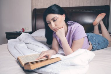 Genç kız yatakta kitap okuyor.