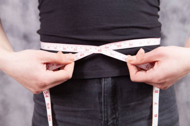 Genç kız, gri bir arka planda karın genişliğini ölçer.