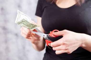 Kadın, dolar banknotunu gri arka planda makasla kesiyor