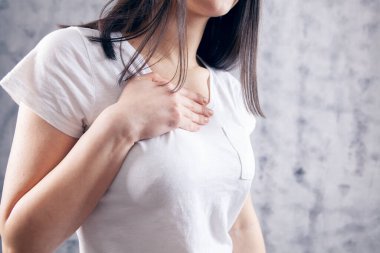 Genç bir kadının gri arka planda kalp ağrısı var.