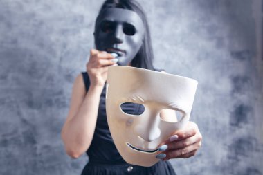 Gri arka planda beyaz ve siyah plastik maske takan kadın.