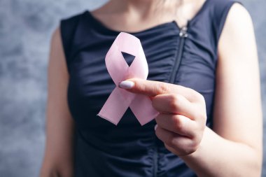 Genç kız gri arka planda pembe bir kurdele tutuyor.