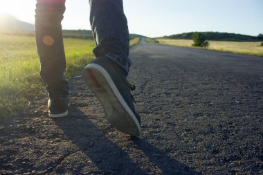 Bir adam gün batımında asfalt yolda yürür.