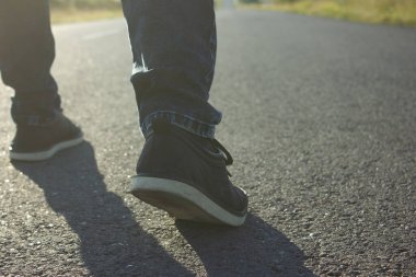 Bir adam gün batımında asfalt yolda yürür.