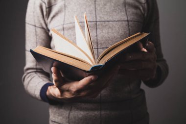 Gri arkaplan üzerine eski bir kitap tutan bir adam.