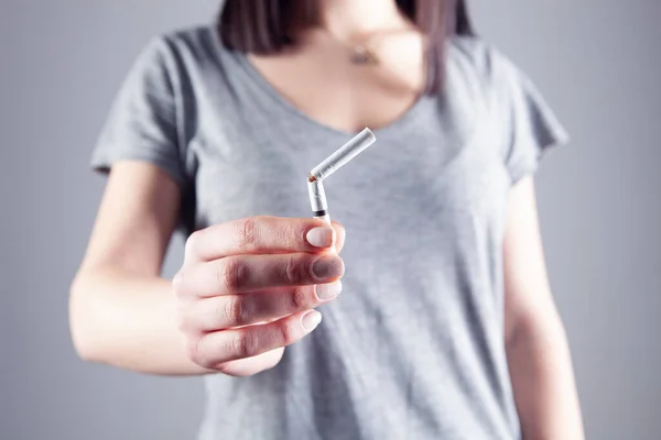 灰色の背景に壊れたタバコを持っている若い女の子 — ストック写真