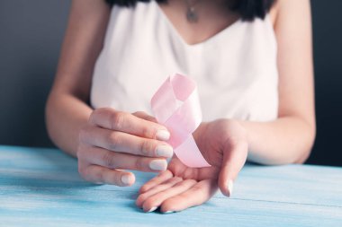 Kadın elleri pembe bir kurdele tutuyor.