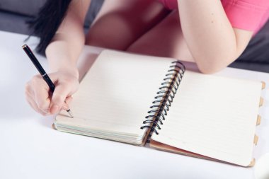 Genç bayan kanepede otururken bir deftere yazıyor.