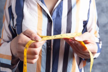 Kadın göğüslerini bir mezura ile ölçüyor.