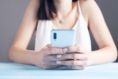 Kadın elleri masada telefonu tutuyor.