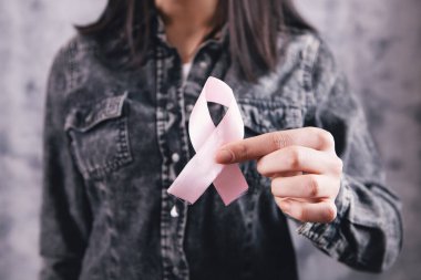 Kadın elleri pembe bir kurdele tutuyor.