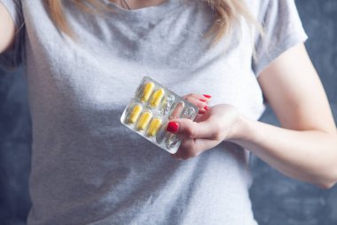 Genç kız gri arka planda haplar tutuyor.