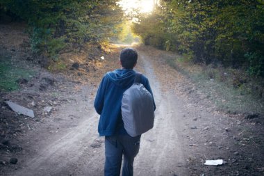 Sırt çantalı bir adam ormanda toprak bir yolda duruyor.