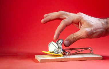 Kırmızı arka planda parası olan bir adamın eli fare kapanında.