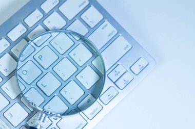 Beyaz arkaplanda büyüteç ve bilgisayar klavyesi, yumuşak odak.