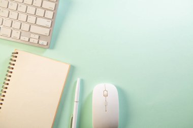 Yeşil zemin üzerinde beyaz bilgisayar klavyesi, fare, defter ve kalem.