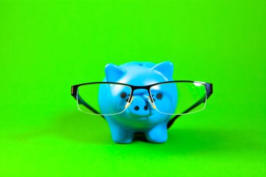 Yeşil arka planda gözlüklü mavi domuzcuk kumbarası. Tasarruf kavramı.
