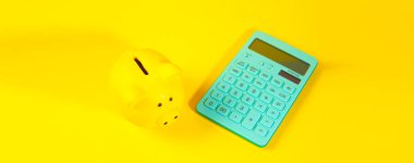 Sarı arka planda hesap makinesi ve domuz kumbarası. Finans ve tasarruf kavramı.