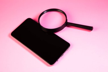 Pembe arka planda büyüteç olan akıllı telefon. Kapat..