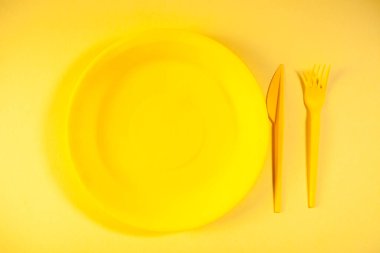 Sarı arka planda boş tabak, çatal, bıçak ve tabak var. yiyecek konsepti.