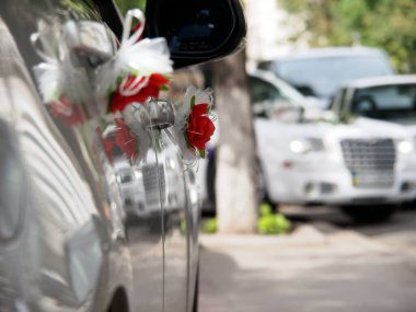 Kar beyazı bir düğün aracının arka planında süslü bir arabanın sapında suni çiçek var.. 