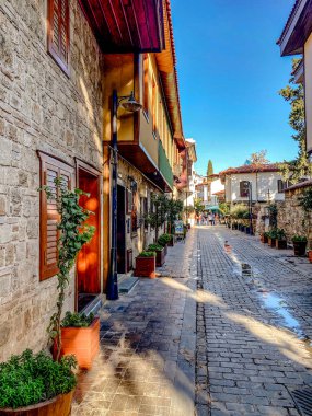 Türkiye 'nin eski Antalya kentinde, Kaleici ilçesinin kaldırım taşı sokağında geleneksel evleri, ahşap balkonları ve açık mavi gökyüzü altında saksı bitkileri var..