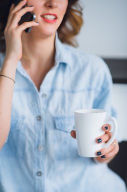 Genç kadının elini Kupası ile bir cep telefonuyla konuşurken Shot görünümü kırpılmış