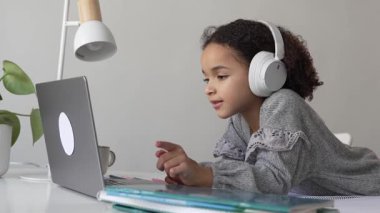 İlkokul Afro-Amerikan öğrenci kulaklıklı el yazısıyla dizüstü bilgisayar kullanıyor. Uzaktan öğrenme çevrimiçi eğitim. Liseli kız evde dijital tabletle çalışıyor.