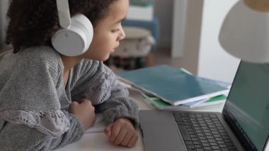 İlkokul Afro-Amerikan öğrenci kulaklıklı el yazısıyla dizüstü bilgisayar kullanıyor. Uzaktan öğrenme çevrimiçi eğitim. Liseli kız evde dijital tabletle çalışıyor.