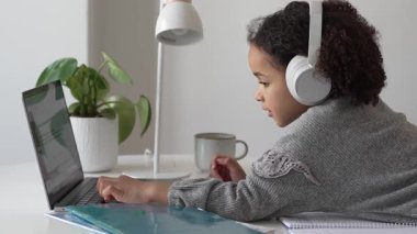 İlkokul Afro-Amerikan öğrenci kulaklıklı el yazısıyla dizüstü bilgisayar kullanıyor. Uzaktan öğrenme çevrimiçi eğitim. Liseli kız evde dijital tabletle çalışıyor.