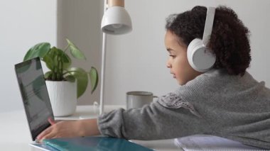 İlkokul Afro-Amerikan öğrenci kulaklıklı el yazısıyla dizüstü bilgisayar kullanıyor. Uzaktan öğrenme çevrimiçi eğitim. Liseli kız evde dijital tabletle çalışıyor.