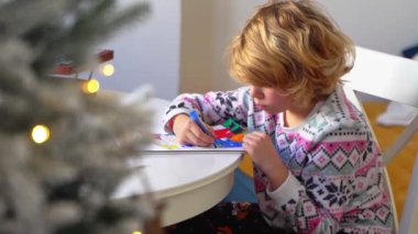 Noel Baba 'ya yeni yıl tatili için mektup yazan çocuk, rahat Noel süslemeleri ve ışıkları, renkli kalemler çizen kız, Noel Baba' ya hediyeler hazırlayan çocuk,