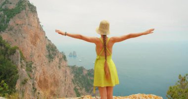 Capri İtalya 'da yaz aylarında Faraglioni kayalarına bakan elbiseli kadın kollarını uzatır..