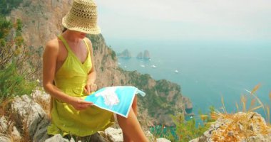 Capri gezisi sırasında elinde Faraglioni 'ye bakan bir haritayla oturan kadın..