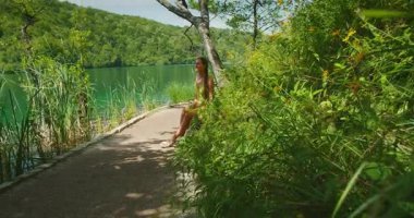 Yaz günü Plitvice Ulusal Parkı 'nda yeşil göl kenarında dinlenen bir kadın..