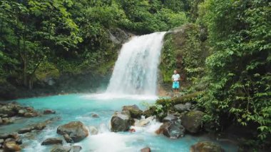 Kosta Rika ormanında turkuaz akan nehir ve şelale havuzu kenarında duran adam..