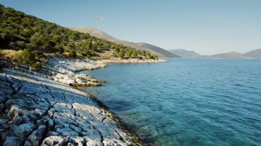 Kefalonya 'da güneşli bir günde ağaçlar ve uzak tepelerle kayalık kıyı şeridi.